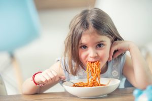 Cute little kid girl eating spaghetti Bolognese at home.
